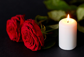 funeral and mourning concept - red roses and burning candle over black background